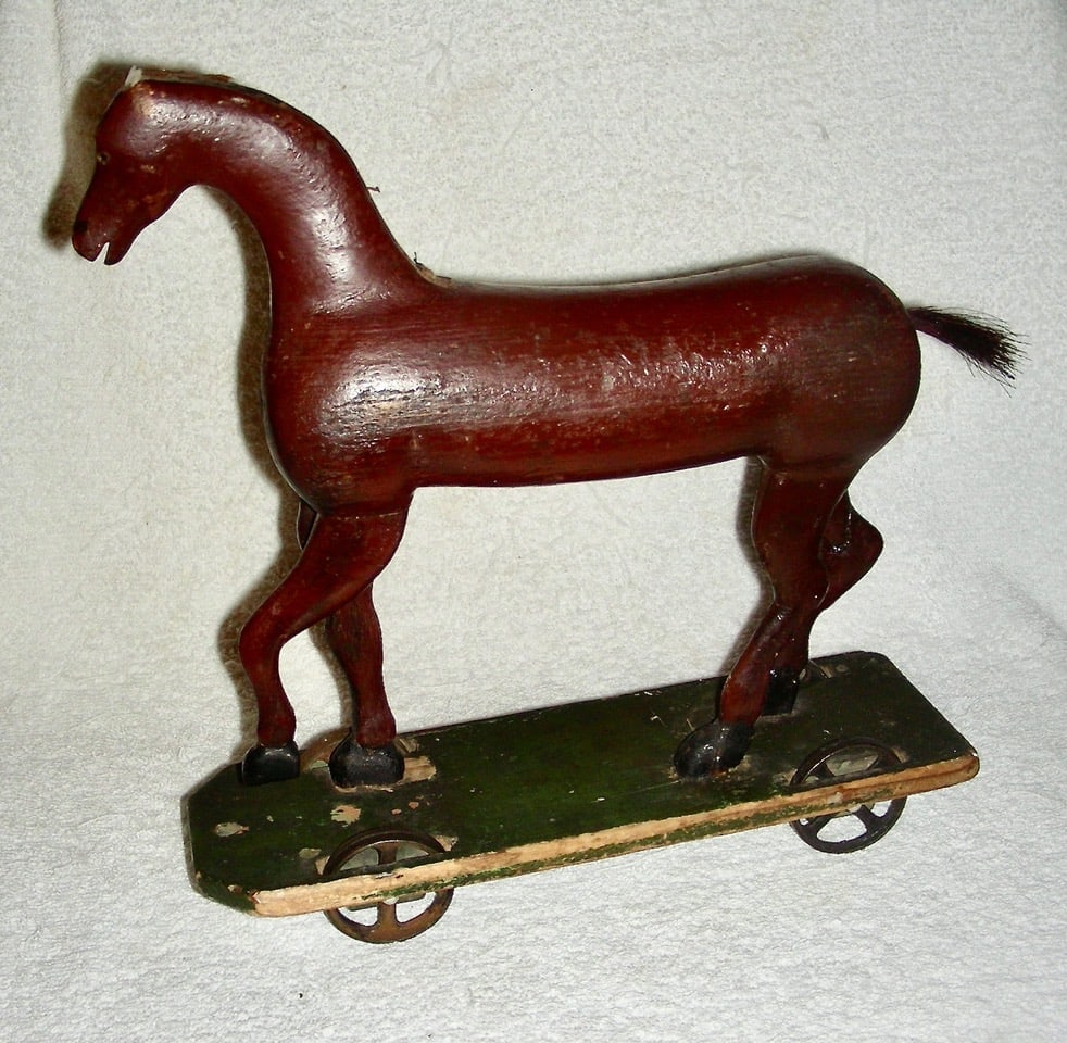 Mid 19th C Primitive Wooden Horse Pull Toy: An early and very sculptural primitive horse pull toy dates to the mid-19th century. Probably carved by a very talented amateur (father for child, possibly), it is mounted on a green painted platform
