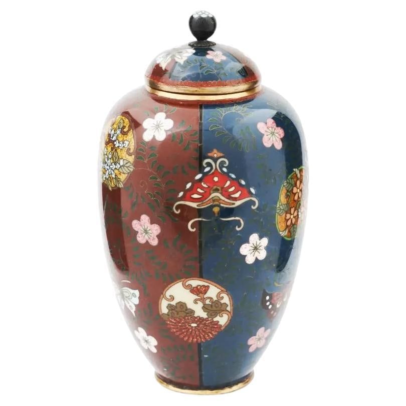 Antique Japanese Meiji Era Cloisonne Enamel Vase: About the Item An antique Japanese Meiji era covered amphora shaped enamel over brass urn vase. The exterior of the vase is adorned with polychrome enameled continuous design of overlapping stylized f