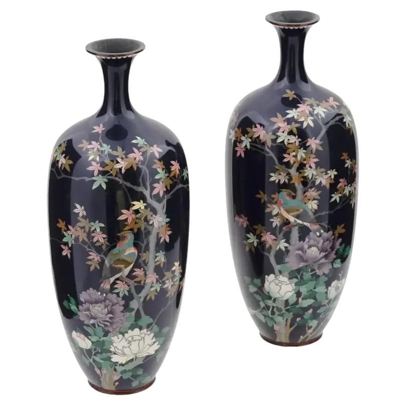 Large Pair of Meiji Japanese Cloisonne Enamel Vase of Birds in a Garden: About the Item A pair of large symmetrical antique Japanese Meiji period enamel over brass vases. Each vase has an amphora shaped body and a narrow neck. Each vase is enameled with a polychrome image