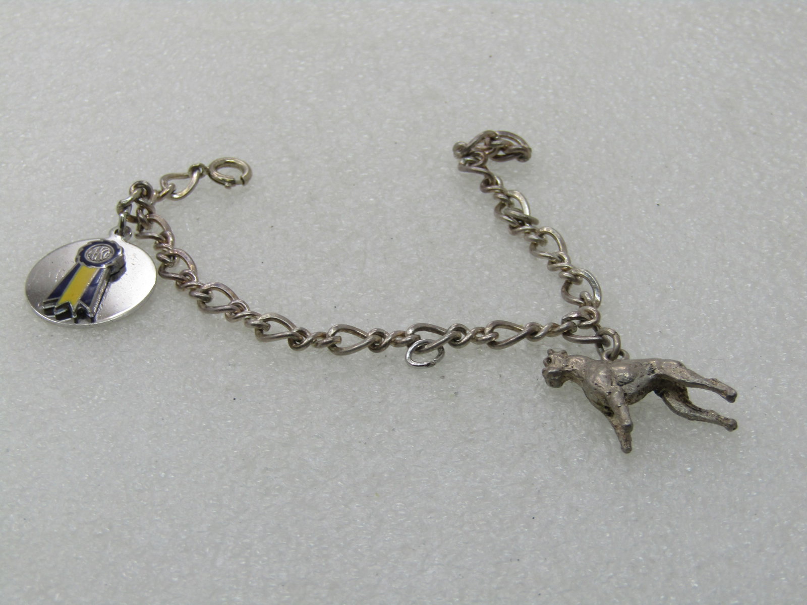 Vintage Sterling AKC & Boxer Charm Bracelet, AKC Ribbon Charm, 7", 14.94 gr.: Vintage Sterling AKC & Boxer Charm Bracelet, AKC Ribbon Charm, 7", 14.94 gr. 5mm wide. The one charm is a blue and yellow AKC Ribbon on a sterling round charm base and the other is a sightly over 1" b
