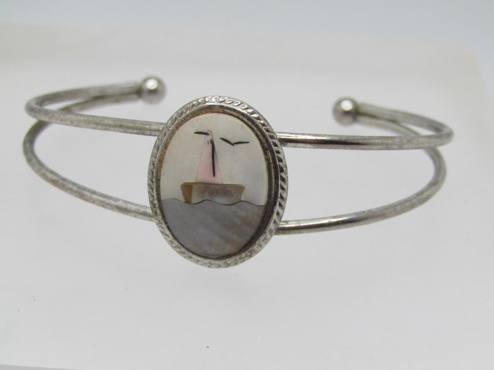 Vintage Inlaid MOP, Beach Scene Cuff Bracelet, 5.75" 1960's-1970's: Vintage Inlaid MOP, Beach Scene Cuff Bracelet, 5.75"-6" 1960's-1970's. Double silver tone round stiff bracelet with opening btween and on top center is a framed inlaid mother-of-pearl sail boat on the
