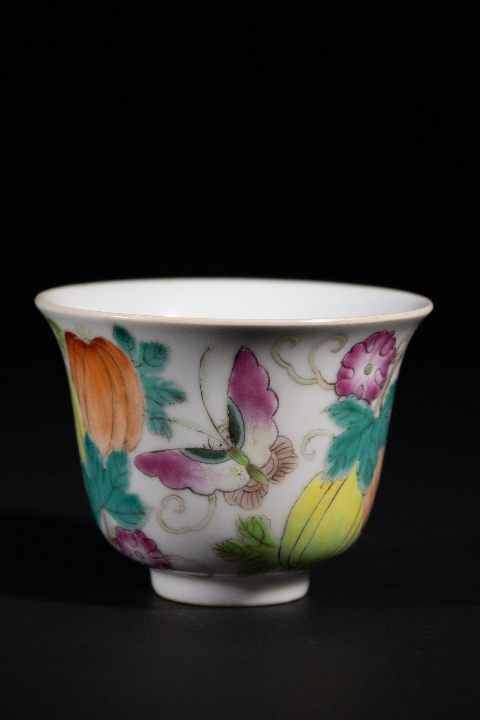 A Chinese Famille Rose Porcelain Cup, Guangxu Mark: A small, flared-rim porcelain cup, decorated with vibrant polychrome enamels in the Famille Rose palette. The decoration features butterflies, gourds, and various flowers amidst subtle scrolling folia