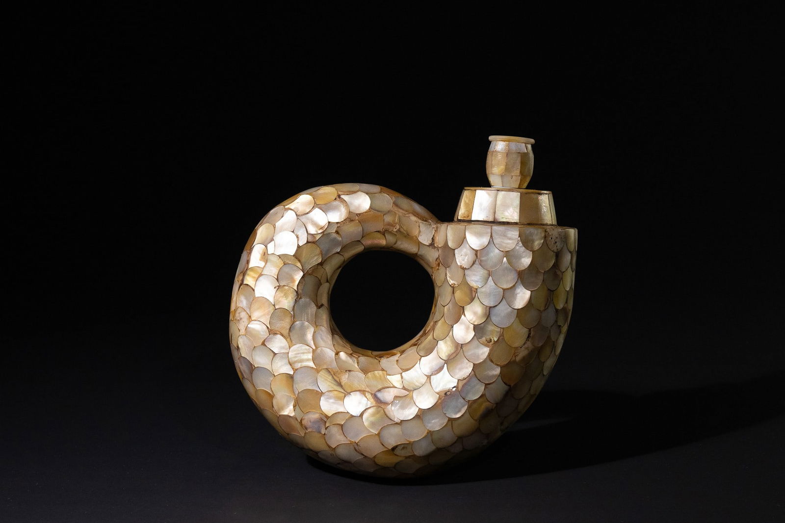 An Indo-Portuguese Mother-of-Pearl Powder Flask, 19th/20th Century: An Indo-Portuguese mother-of-pearl powder flask. This decorative, curvilinear vessel is shaped like a stylized looped or C-shaped form, featuring a central circular perforation and a single, flared ro