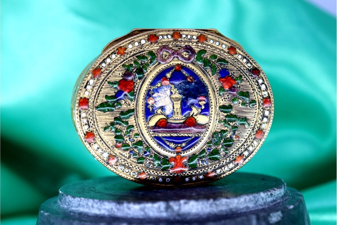 Elliptical gold pill box with enamel reliefs, engraved floral motifs and friezes with bands along: Title:Elliptical gold pill box with enamel reliefs, engraved floral motifs and friezes with bands along the length involving natural and musical elements Description:Description: Elliptical gold pill