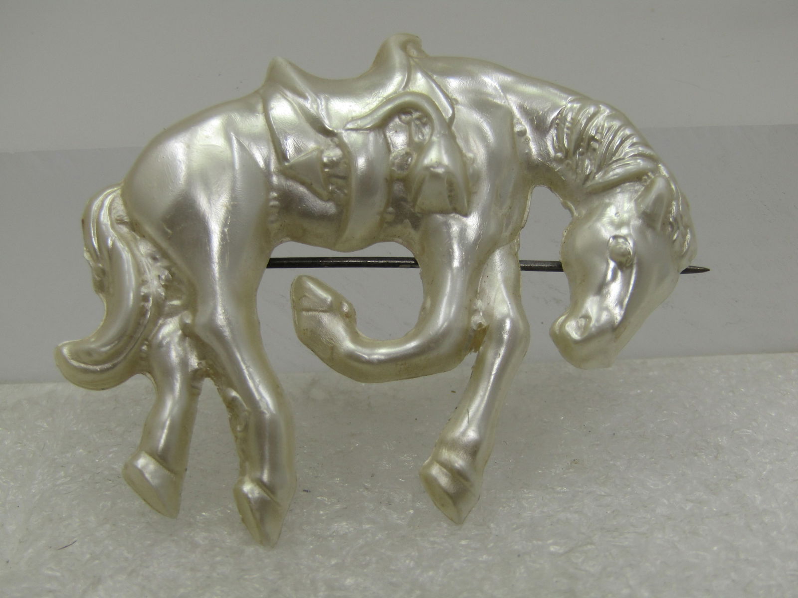 Vintage Celluloid Horse/Bucking Bronco Brooch, 1940's: Vintage Celluloid Horse/Bucking Bronco Brooch, 1940's. Pearly white with a saddle and horse in a bucking pose. It is appx. 2" by 1.75. Plastic c-clasp. Very good condition. Great for rodeo and equine