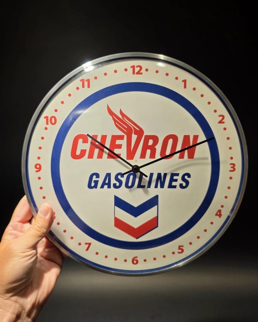 Round Chevron Gasoline Oil Wall Clock Sign: 12" Wonderful reproduction vintage-style Chevron Gas and Oil round clock. The clock face features the Chevron logo prominently in the center, with the word "CHEVRON" in red and "GASOLINES" in blue. Th