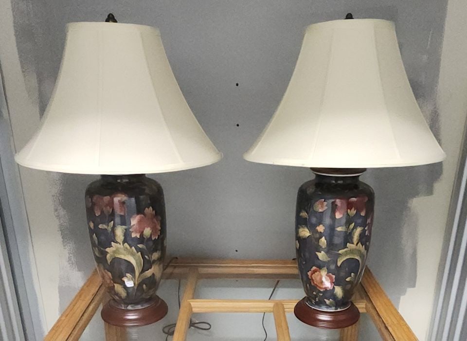 Pair of vintage Hollywood Regeny style hand-painted porcelain lamps representative of Scully &: These elegant lamps feature richly detailed porcelain bodies with a floral motif on a black lacquer-style base. They have delicate gilt accents highlighting the flowers and foliage, with fine crackle