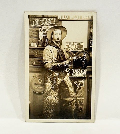 Photo Postcard of A Cowboy in a Saloon: Title: Photo Postcard of A Cowboy in a Saloon Description: A real postcard photograph of a man dressed in his finest cowboy outfit in a saloon festooned with fun sayings. 'Wild West Bar', 'No Place fo