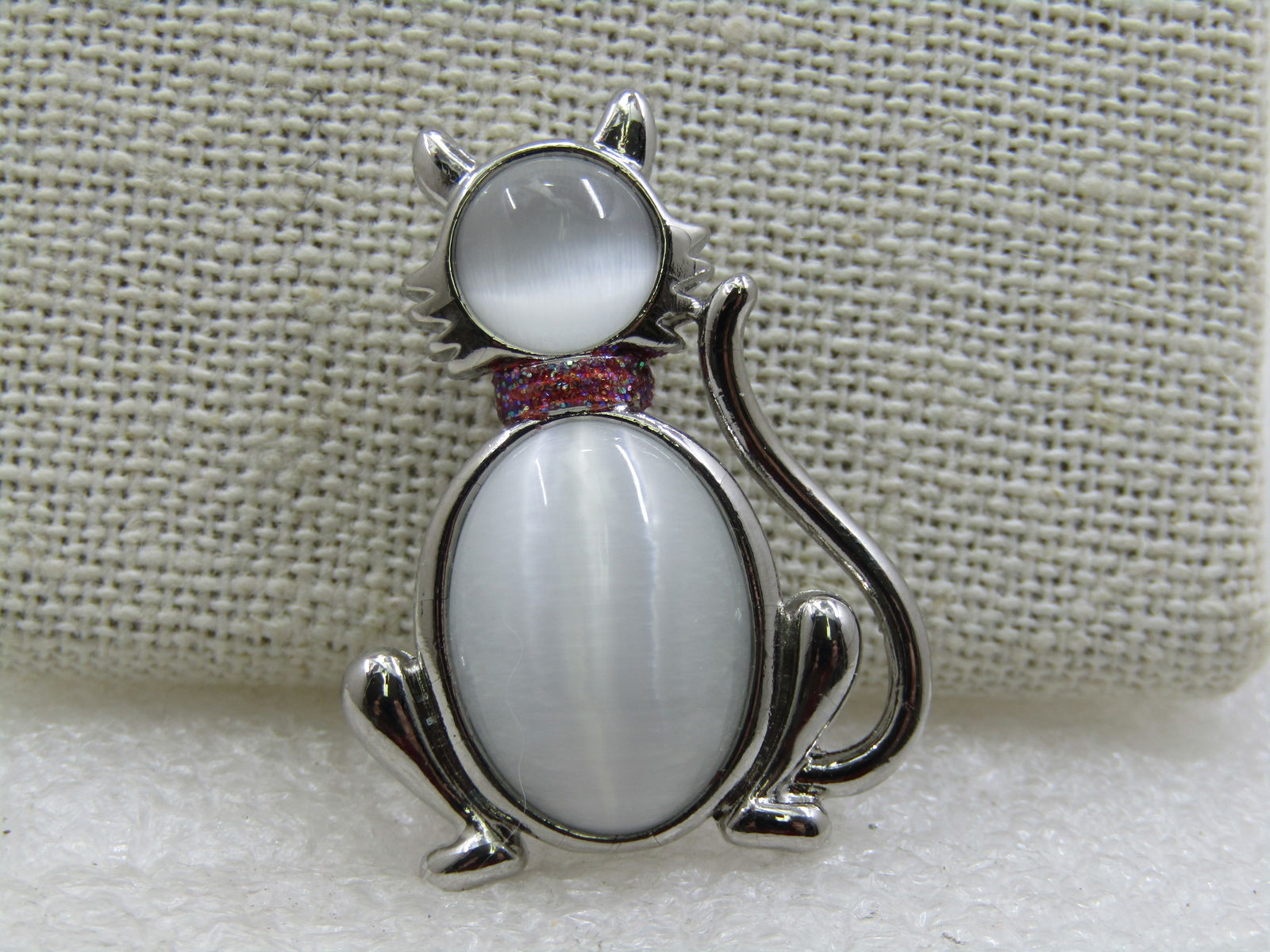 Vintage White Moonstone Cat Brooch, 1.5" by 1".: Vintage White Moonstone Cat Brooch, 1.5" by 1", 1960's-1980's. Silver tone with a white round and oval moonstone that is appx. 8mm round for the face and 16mm by 12mm for the body. Pink enameled glitt