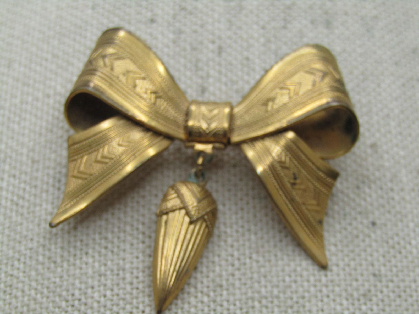 Victorian Bow Brooch with Dangling Fob, C-Clasp, 1800's-1910.: Victorian Bow Brooch with Dangling Fob, C-Clasp, 1800's-1910. This is gold tone me tal with a long pin that the point extends slightly beyond the loop of the bow. it is a 3-D bow, pressed metal with a