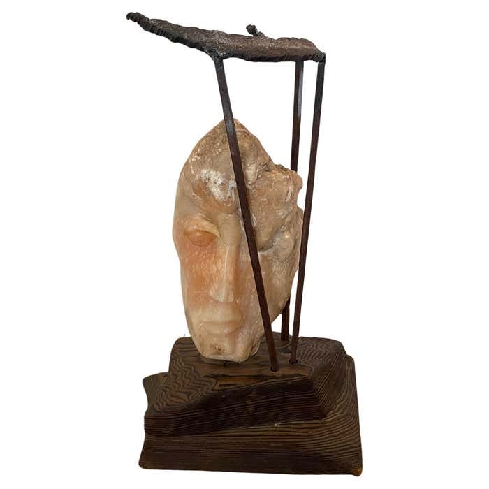 Metal Framed Alabaster Face Sculpture on Wood Base by Leon Saulter: Title: Metal Framed Alabaster Face Sculpture on Wood Base by Leon Saulter Description: This marble sculpture, signed Leon Saulter, dated 1966, presents a stylized human face carved in light-toned ston