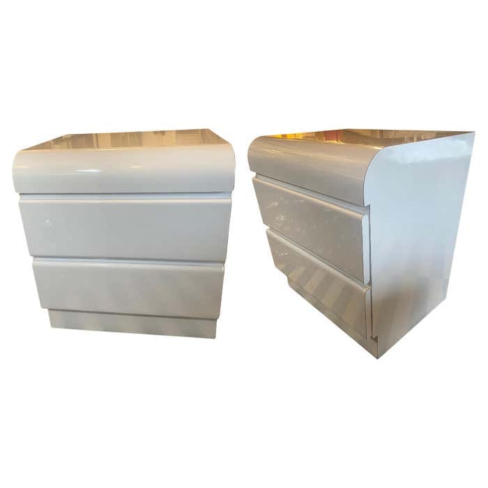 Pair of Modern White Laminate Nightstands: Title: Pair of Modern White Laminate Nightstands Description: This postmodern white gloss laminate nightstand, circa 1980, features a sleek waterfall-front design with two drawers on smooth metal glid