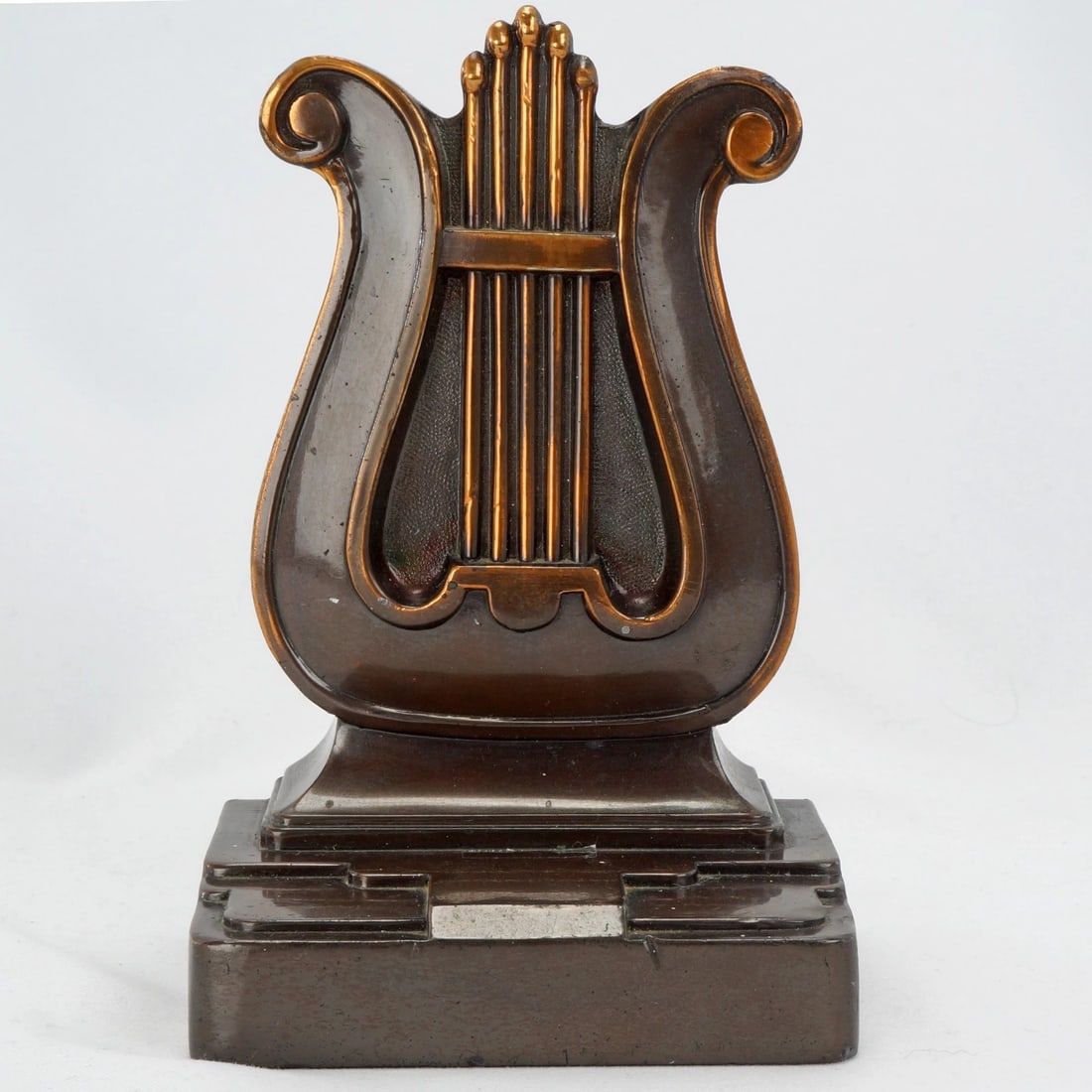 Single Art Deco Lyre Bookend PM Craftsman: Title:Single Art Deco Lyre Bookend PM Craftsman Size:3 ½ in (8.9 cm) wide x 2 ½ in (6.4 cm) deep x 5 ½ in (14.0 cm) tall. Description:A heavy copper-clad bookend modeled of a lyre