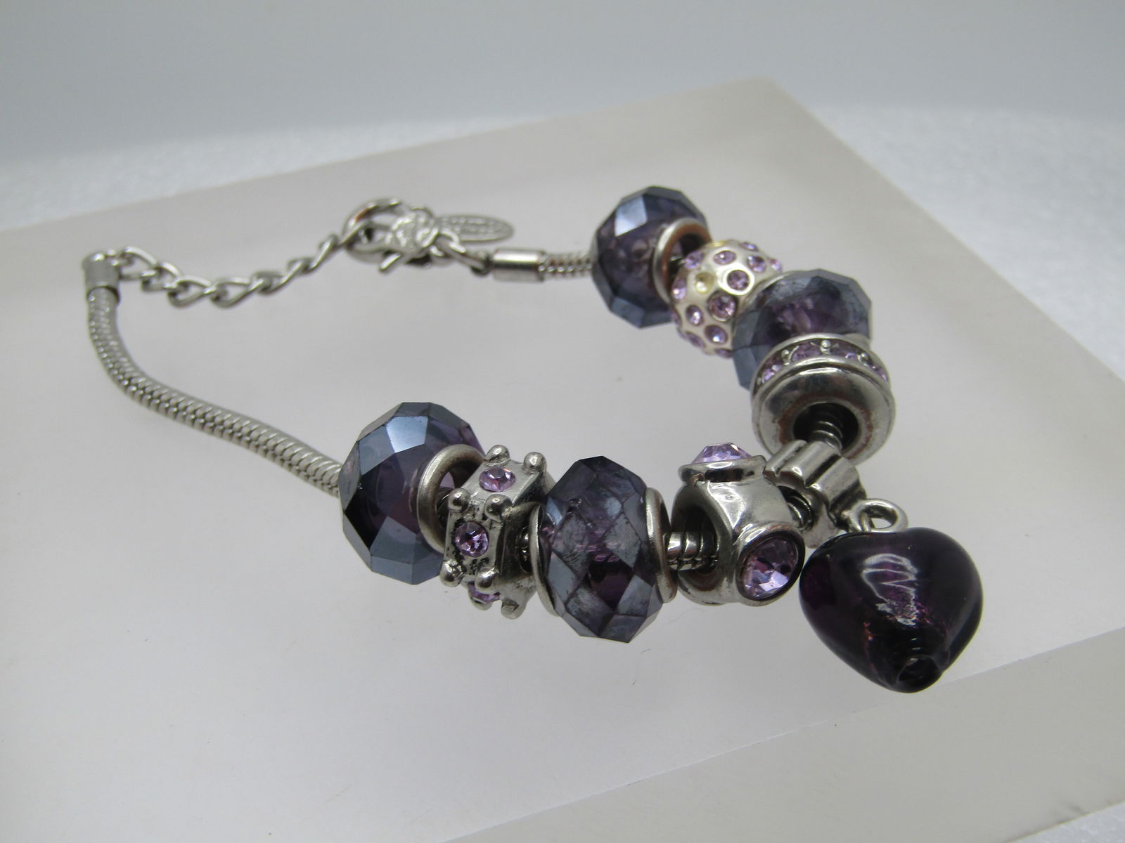 Purple Heart Beaded & Rhinestone Slide Bracelet, Charmed Feelings, 7"-8.5", 1980's-1990's: Purple Heart Beaded & Rhinestone Slide Bracelet, Charmed Feelings, 7"-8.5", 1980's-1990's. The main drop is a purple glass heart. There are four faceted purple slide beads and a wide silver tone bead