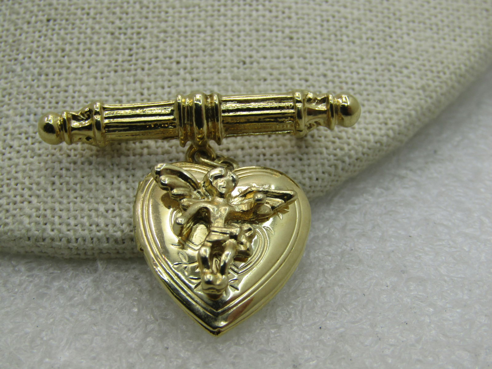 Gold tone Angel Heart Locket Brooch: Gold tone Angel Heart Locket Brooch, 1.5" wide and 1-3.8" height. Looks new, hinged locket that will hold two photos - hovering angel on coper. Locket is heart-shaped. Very good, new condition. (INV.