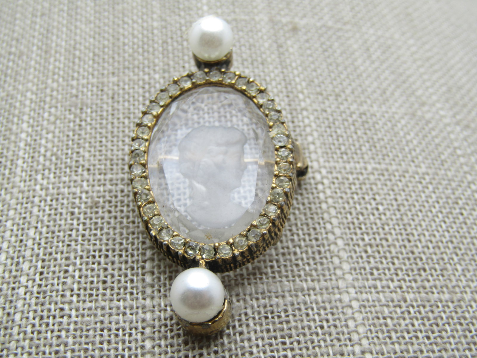 Vintage Reverse Cameo in Glass/Crystal Brooch, , Rhinestones & Faux Pearls, 1960's-1970's: Vintage Reverse Cameo in Glass/Crystal Brooch, , Rhinestones & Faux Pearls, 1960's-1970's. It is 1.75" tall and 7/8" wide with a halow of clear stones set in the gold tone setting creating a halo arou