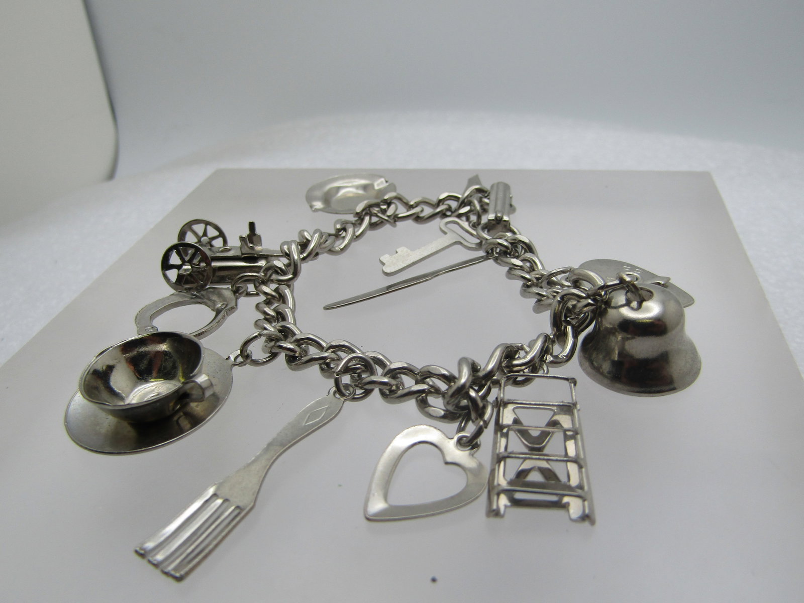 Vintage Charm Bracelet 7", 11 Charms, Heart Spinner, Bell, Ladder, Cup Saucer, More: Vintage Charm Bracelet 7", 12 Charms, Heart Spinner, Bell, Ladder, Cup Saucer, Key, Ashtray, Handcuffs, Fork, Open Heart, Knife. Silver tone. Flip clasp Not signed by the maker. 1960's. Very good cond