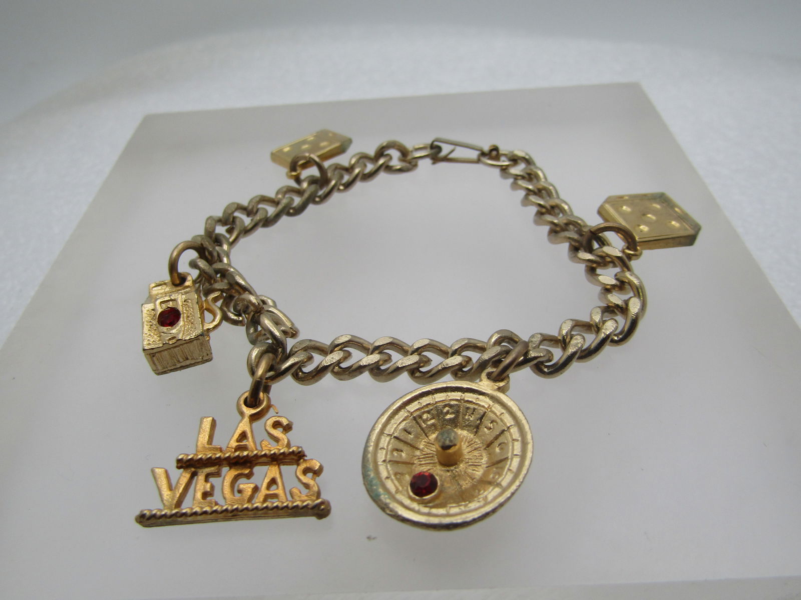 Vintage Las Vegas Charm Bracelet, 1960's-1970's, 7": Vintage Las Vegas Charm Bracelet, 1960's-1970's, 7" - God tone with a 5.5mm wide curb link chain and flip clasp and five charms, two dice, slot machine with red rhinestone, Las Vegas, and Roulette whe