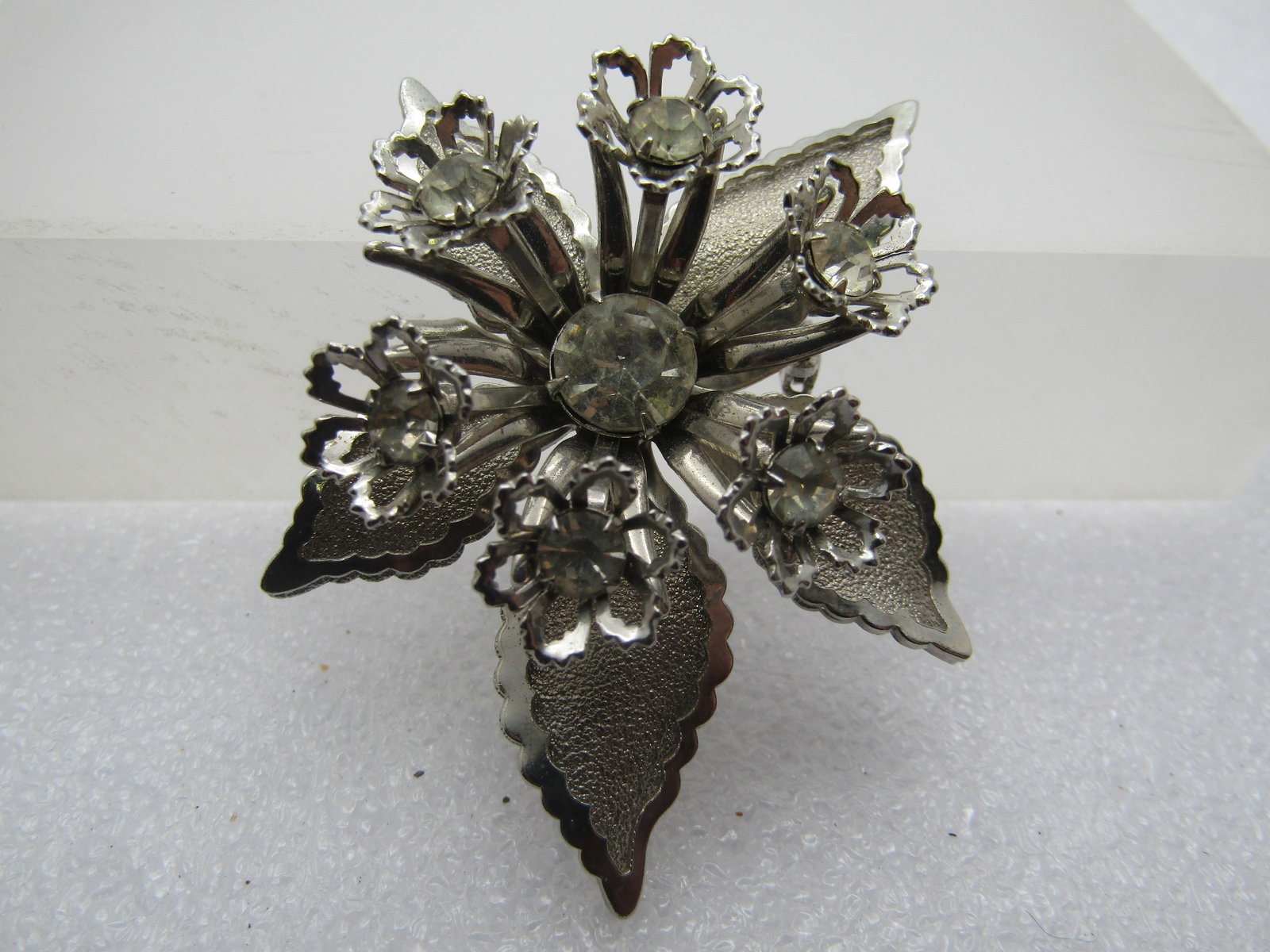 Vintage Rhinestone Orchid Blossom Brooch, 1960's-1970's: Vintage Rhinestone Orchid Blossom Brooch, 1960's-1970's. Silver tone with a recessed center appx. 8mm clear rhinestone and six raised mini blossoms with filigree petals and recessed in the center of t