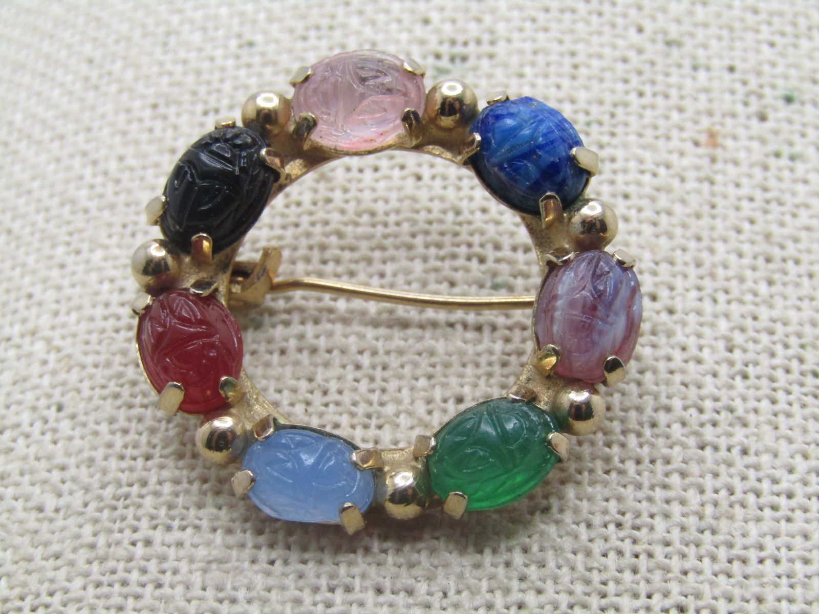 Vintage Scarab Circle Brooch, 1960's-1970's, 1-1/8": Vintage Scarab Circle Brooch, 1960's-1970's, 1-1/8". Pressed glass scarabs simulating rose quartz, onyx, carnelian, jade, amethyst, sodalite, and blue and white quartz. It is gold tone and the stones