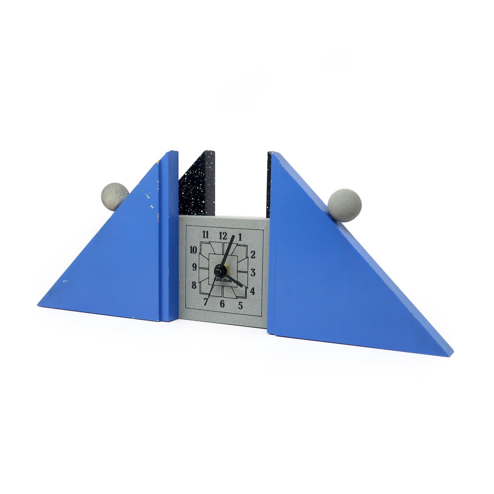 1980s French Postmodern Mantle Clock: A sculptural French postmodern mantel clock with blue and splatter painted supports, gray face and accents, and black numbers and hands. A fantastically contrasting low triangular shape with round det