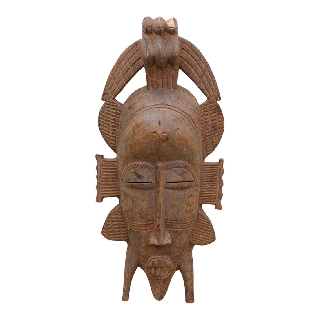 Vintage Fierce Guardian Senufo Mask: This imposing Senufo Kpelie mask from the Ivory Coast is a striking example of African tribal art. The mask is characterized by its large size, fierce expression, and elaborate headdress. The surface