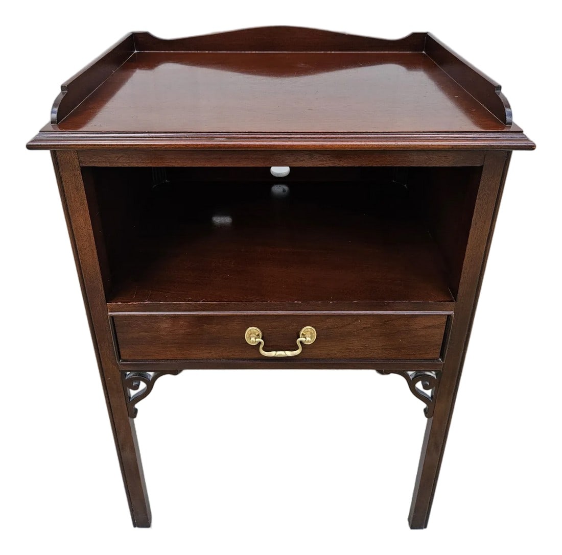 Councill Craftsmen Mahogany Chippendale Nightstand: A Chippendale style mahogany nightstand by Councill Craftsmen. This piece features one drawer and open storage. The top has a lip around the back and sides. The apron or base of the stand has fretwork