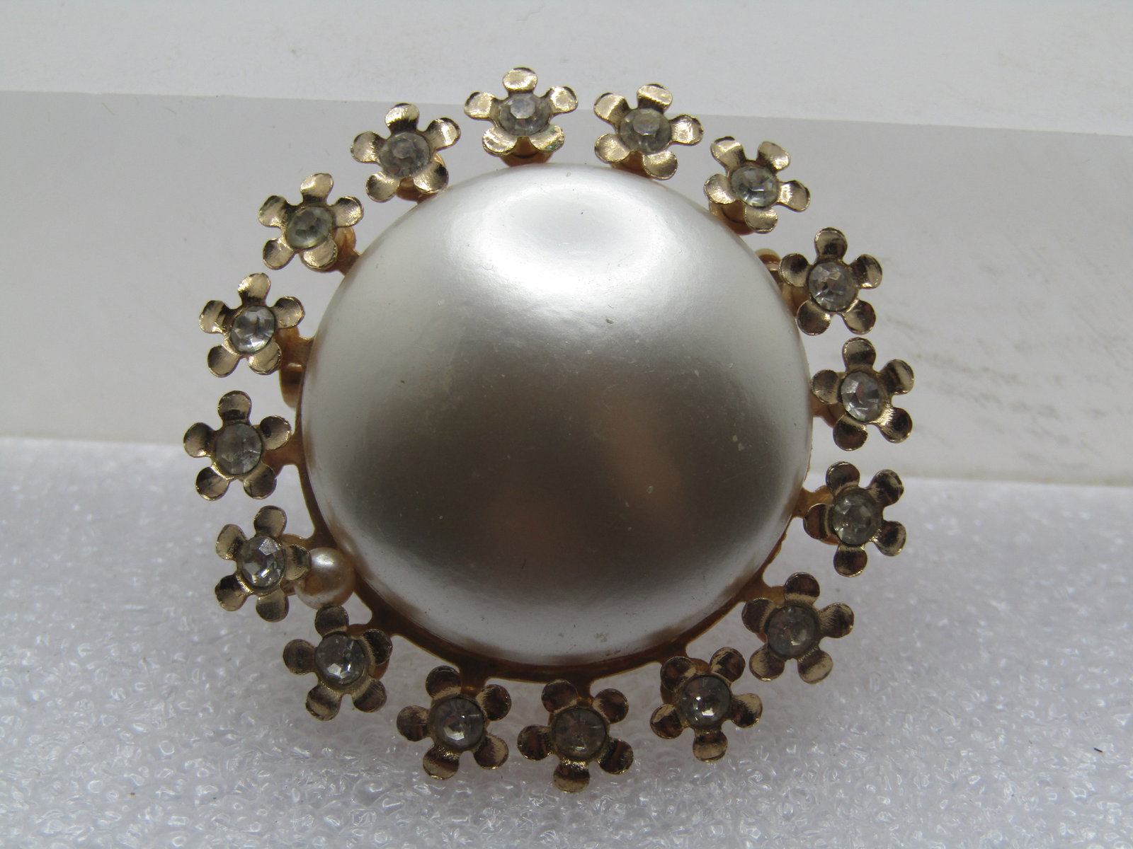 Vintage Faux Pearl Blossom Halo Brooch, Rhinestones, 1970's-1980's: Vintage Faux Pearl Blossom Halo Brooch, Rhinestones, 1970's-1980's. The brooch has a domed slightly off white faux pearl button top that is appx. 1" across. Around that is a halo of forget-me-not
