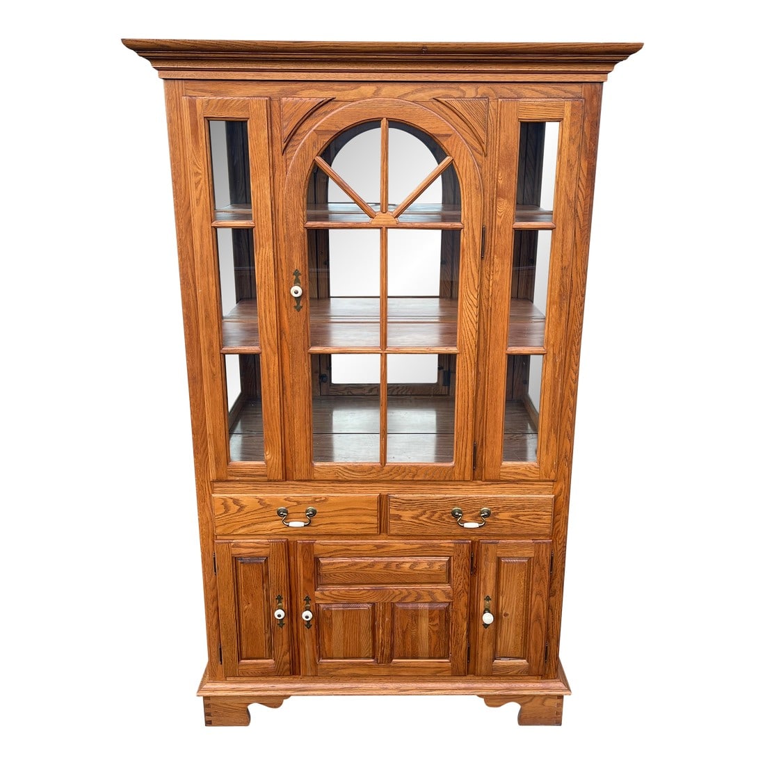 Keller Illuminated Oak China Display Hutch Cabinet: Oak China cabinet made by Keller Furniture in the late 20th century. A beautiful body with cathedral wood grill windows and mirror backing. Evidence of replaced shelving in main display body and botto