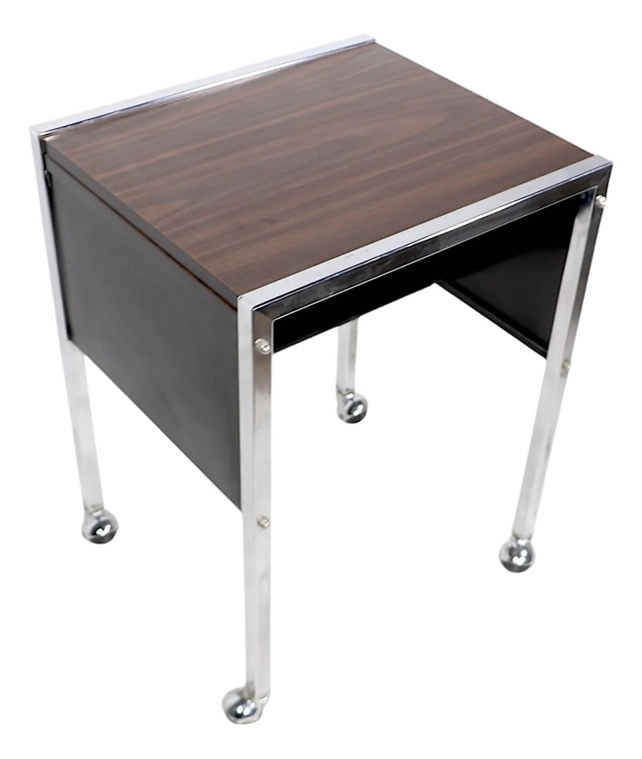 Mid Century Office Cart Rolling Table C. 1970's: Chic rolling cart, side table stand, featuring a faux wood formica top, supported by a squared chrome frame, with black panel sides, back and interior. The interior has a lower half shelf, the feet