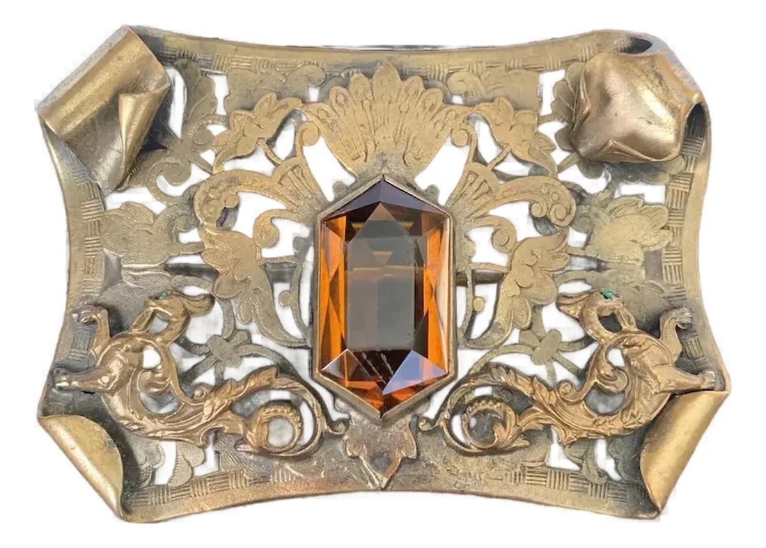 Late 19th Century Victorian Dragon Sash Pin: Gorgeous brass Victorian sash pin featuring a citrine glass stone in the center. The pin is flanked on either side by a dragon, each with a glimmering, green, glass eye. Citrine glass stone has