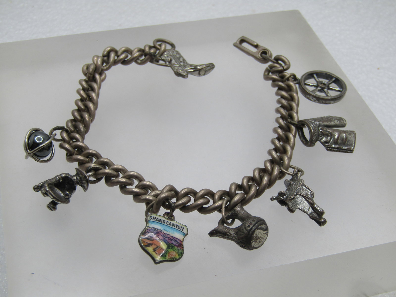 Vintage Sterling Charm Bracelet, Western Themed, 7.75" 1940's-1950's: Vintage Sterling Charm Bracelet, Western Themed, 1940's-1950's. 7.75". This has an older swivel style clasp with a 6.5mm wide heavy curb link chain. There are eight charms: wagon wheel; chaps; saddle;