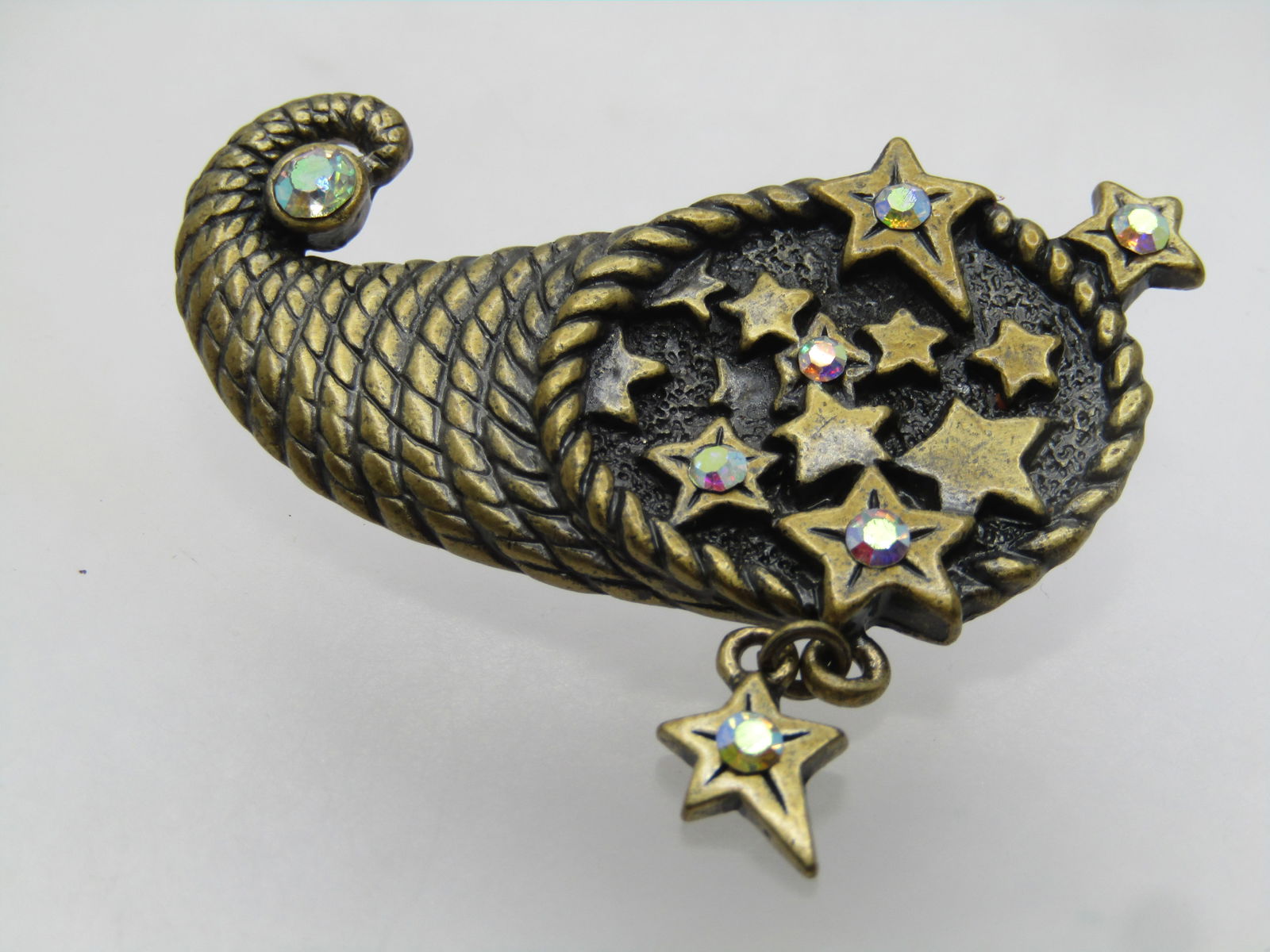 Vintage Cornucopia Brooch Brooch, AB Rhinestone Stars. Dangle, Signed DD. 1980's: Vintage Cornucopi Brooch, AB Rhinestones in Stars with a dangle one too. Brassy tone. Stars inside the opening of the cornucopia - some with aurora borealis rhinestoness and one wrapped at the tip. Si