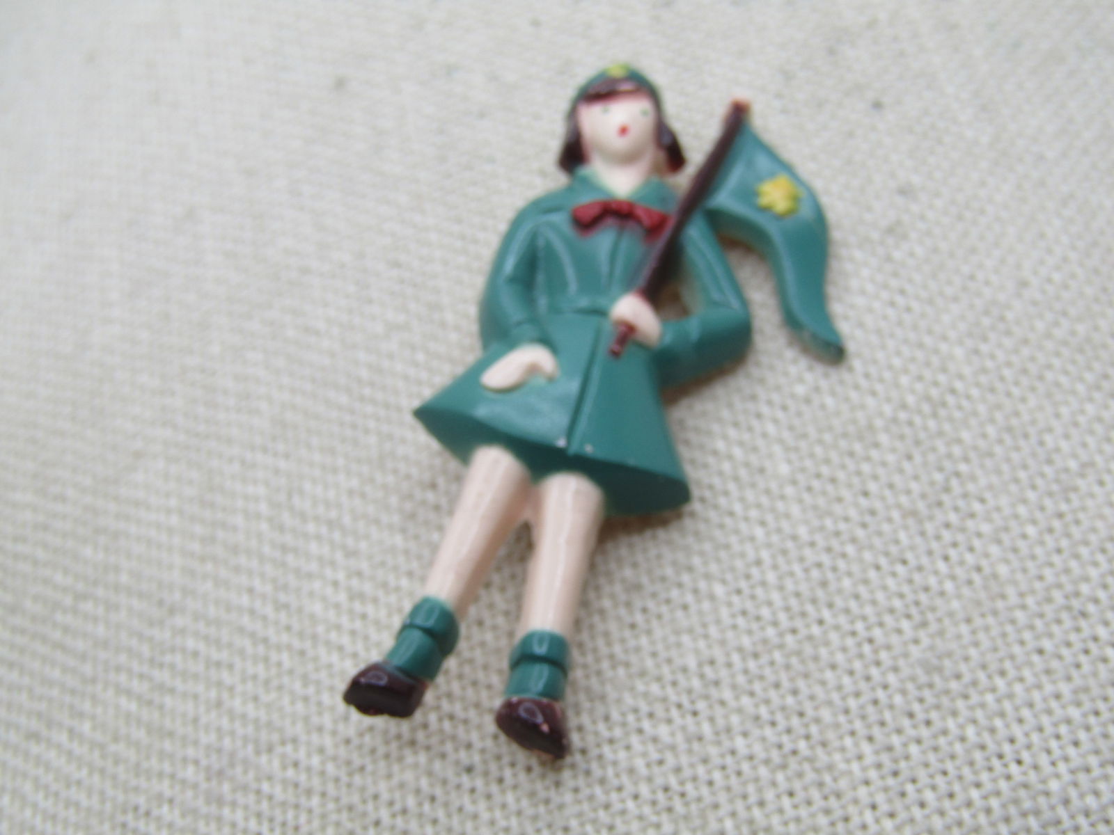 Vintage Girl Scout with Flag Plastic Brooch, 1940's: Vintage Girl Scout with Flag Plastic Brooch, 1940's. Plastic brooch with a girl scout with brown hair, green uniform, flag, hat, and socks, with red bow tie. Brown shoes. Yelow Girl Scout markings. It