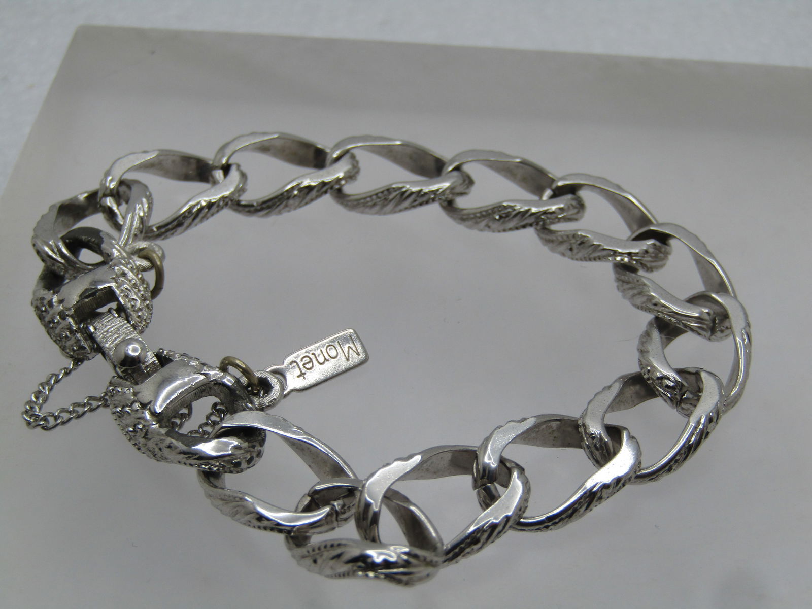 Vintage Monet Charm Bracelet, 7.25", 1960's, Safey Chain, Signed: Vintage Monet Charm Bracelet, 7.25", 1960's, Safey Chain, Signed. This has decorative silver tone links with a design on the outer sides. It is appx. 10.5mm wide. It has a flip clasp with a textured a