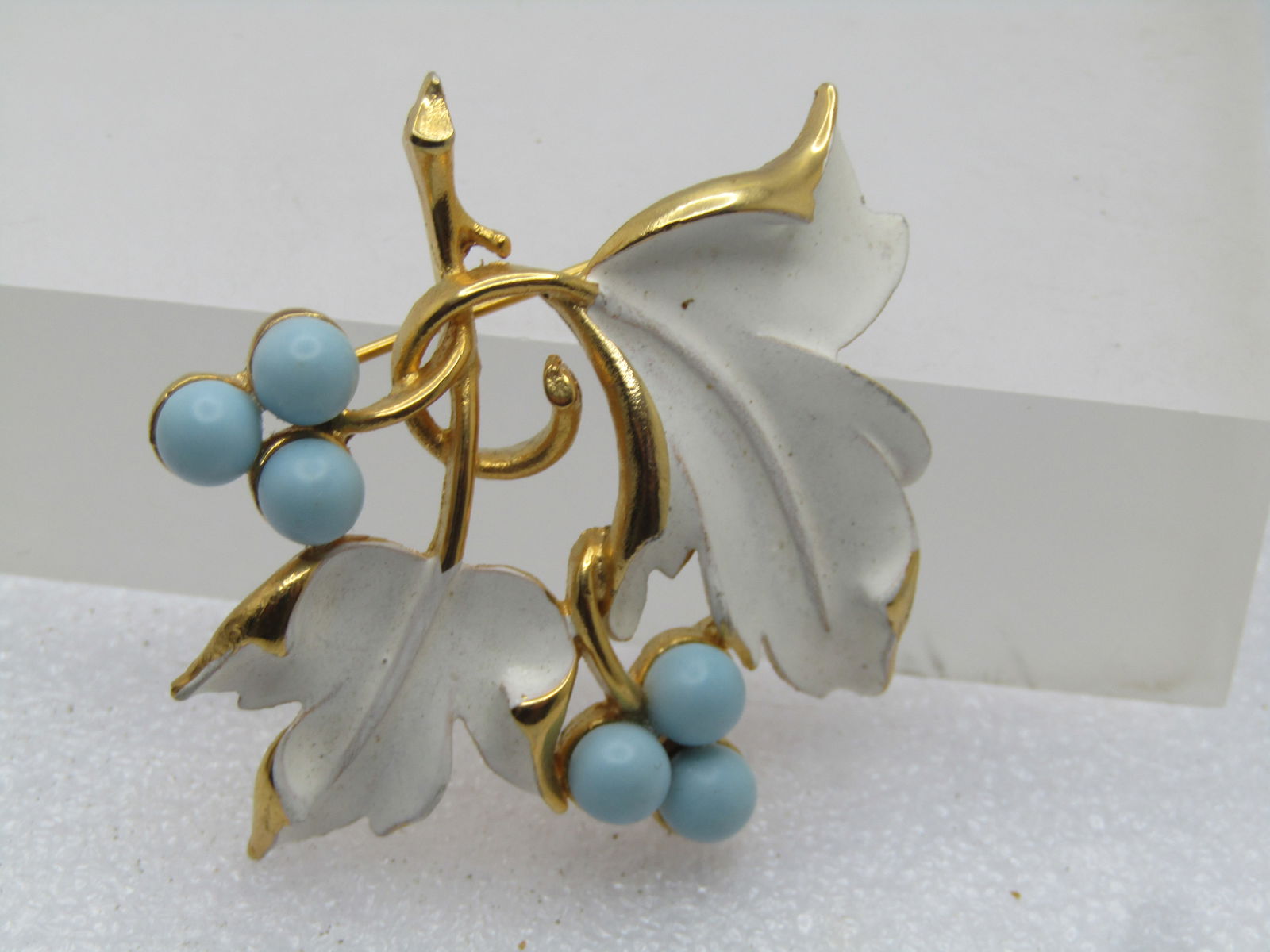 Vintage White Enameled Leaf Brooch, Blue Beads, Signed Sarah Cov. 1960's-1970's: Vintage White Enameled Leaf Brooch, Blue Beads, Signed Sarah Cov. 1960's-1970's. The brooch has two white enameled leaes with gold tone stems and setting. There are two sets of three 5.5mm beads
