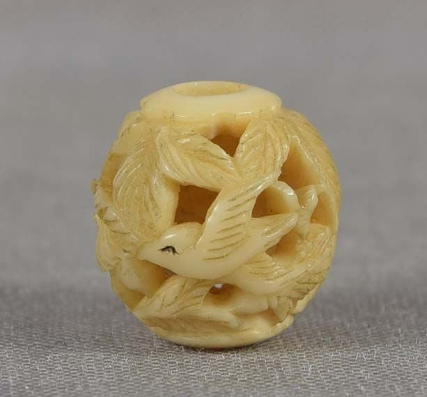 19c marine OJIME netsuke slide BIRD & CHRYSANTHEMUM: 19th century small marine material ojime (slide bead for tightening the cord going from netsuke to inro) carved and perforated in the round with a bird in flight by chrysanthemum flower with leaves. W