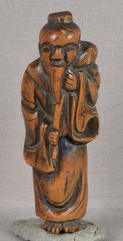 18c netsuke SENNIN with fly whisk: Late 18th century boxwood netsuke of a sennin (Chinese sage) holding a hossu (fly whisk) on his shoulder. Nice early carving, chips here and there, clever himotoshi (cord opening) through the sleeve