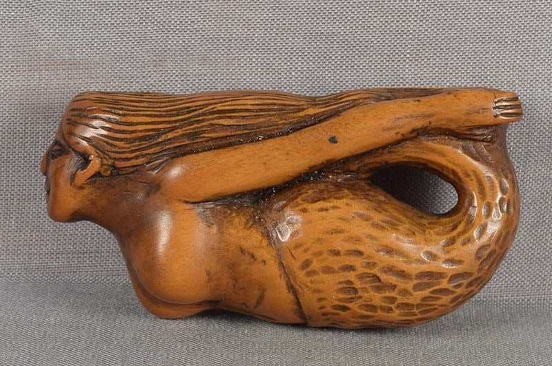 19c netsuke STRETCHING MERMAID: Late Meiji (1890s to 1910s) boxwood netsuke of a mermaid stretching as she bends her tail up and holding it with her hands. Unusual subject, nicely carved, pleasant wear and patina. Length 2.35