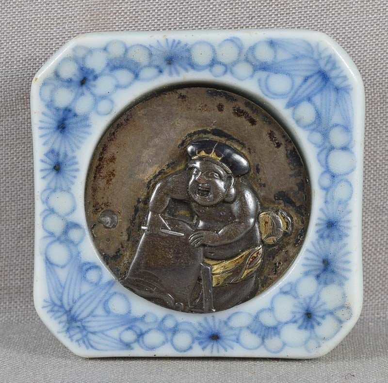 19c metal & porcelain netsuke DAIKOKU SHAVING head of FUKUROKUJU: Rather unusual 19th century netsuke in kagamibuta (mirror lid) style with multimetal disc depicting Daikoku on a ladder shaving the head of Fukurokuju, and porcelain bowl with underglaze blue