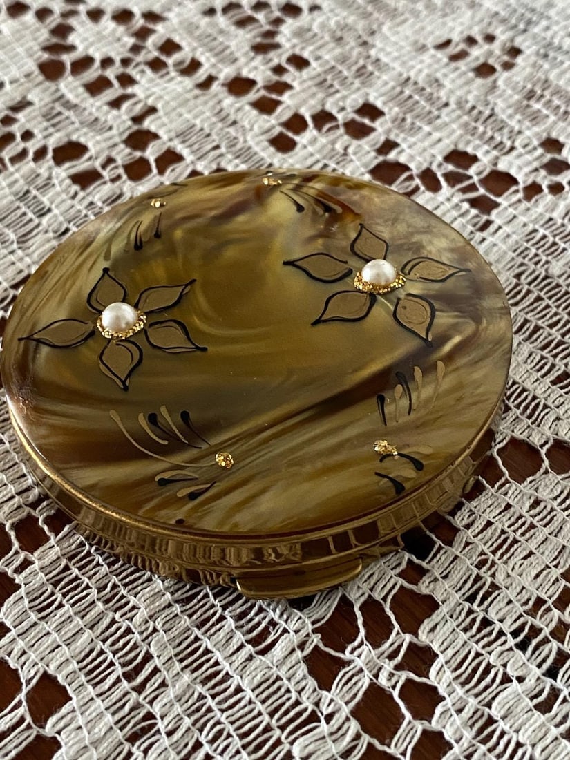Vintage 1950s Powder Compact Faux MOP + Rhinestones: Vintage from the 1950s Materials: Metal, plastic Lucite to look like mother of pearl Kind of a golden butterscotch Rhinestone flowers, maybe stylized plumeria Round Brasstone Mirror, interior