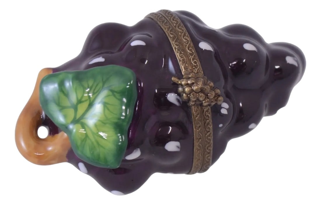 Limoges Purple Grape Cluster Trinket Box: Hand painted Limoges of France trinket box designed as a deep purple grape cluster accented with a green leaf and goldenrod stem has a brass grape cluster closure. Maker's mark on interior. Light