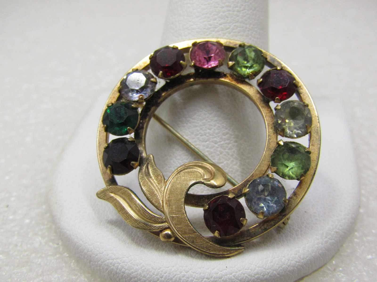 Vintage Van Dell 12kt G.F. Rhinestone Circle Brooch, 1940's-1960's: Vintage Van Dell 12kt G.F. Rhinestone Circle Brooch, 1960's. This has a mix of green, red, clear pink and blue 5mm round glass faceted stones and a curved leaf accent. The brooch is 1.25" tall and