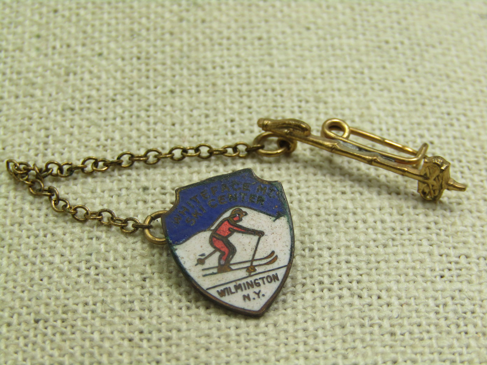 Vintage Enameled Pin, Whiteface Mt Ski Resort, , NY: Vintage Enameled Pin, Whiteface Mt Ski Resort, Wilmington, NY. 1950's Enameled sking scene on shield shape with chain and ski powl pin attached. Enameled in blue, white, and red. It is gold filled. Th