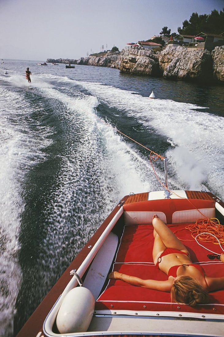 Slim Aarons Official Estate Print - Leisure In Antibes: 1969 (printed later): Title: Slim Aarons Official Estate Print - Leisure In Antibes: 1969 (printed later) Description: Slim Aarons Estate Print - Leisure In Antibes 1969 A woman sunbathing in a motorboat as it tows a