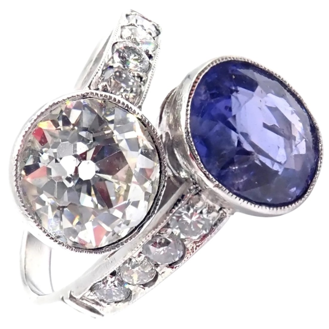 Vintage Estate Platinum Diamond Sapphire Art Deco Crossover Ring: Vintage Art Deco platinum crossover ring featuring a dazzling old European-cut diamond paired with a rich blue sapphire. Milgrain edging and graduated side diamonds enhance its geometric elegance. A s