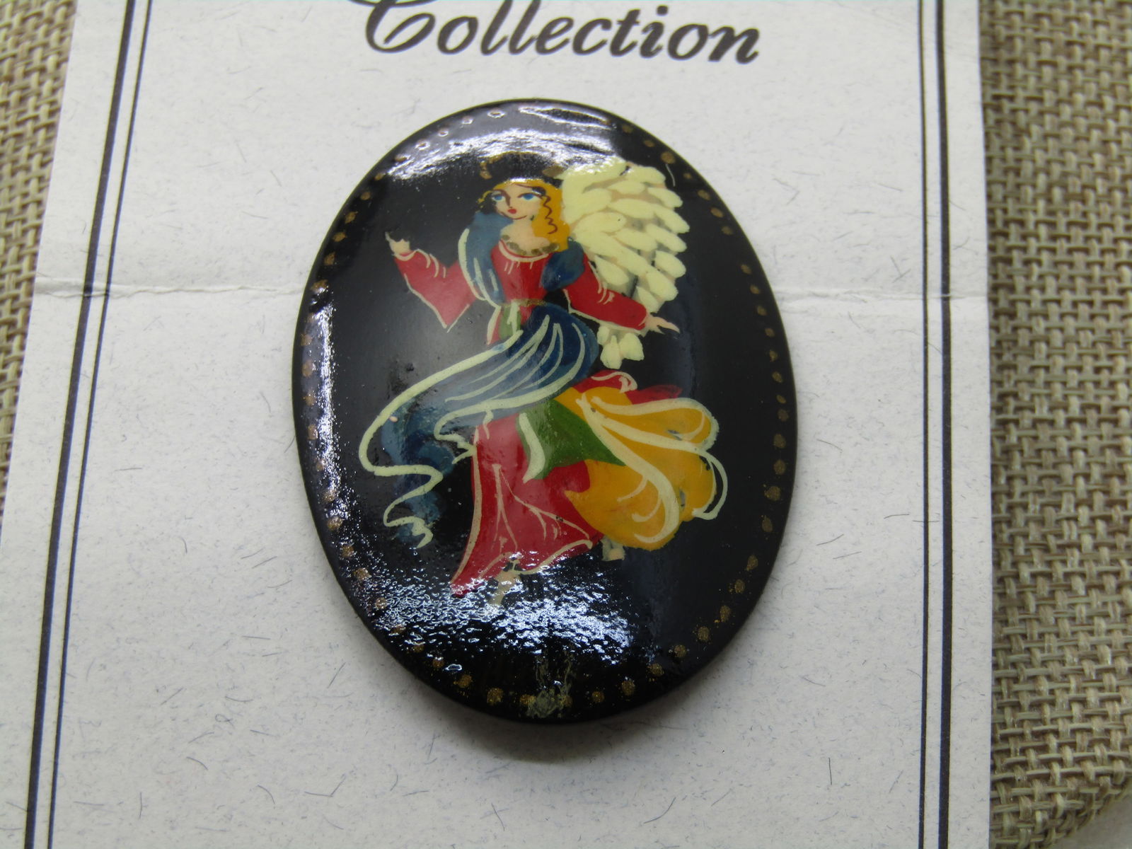 Vintage Russian Black Lacquered Angel Brooch, Oval 2.25" tall by 1.5", Vintage new on card.: Vintage Russian Black Lacquered Angel Brooch, Oval 2.25" tall by 1.5". Painted Angel in red, blue, green, and golden yellow with flowing gown, white wings, blonde hair. Vintage new on The Russian Coll