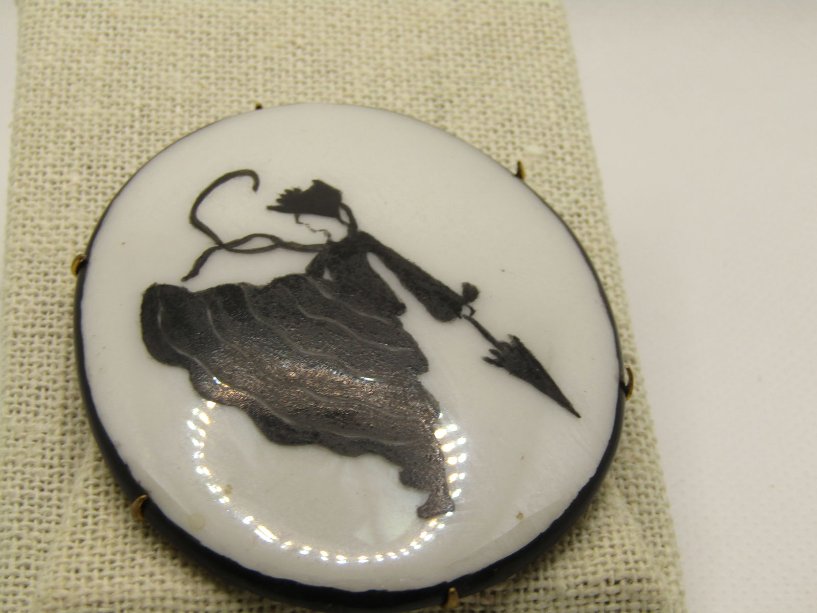 Vintage Early 1930's Black & White Lusterware Brooch, Woman with Umbrella 2.5" by 2": Vintage Early 1930's Lusterware Black & White Painted Brooch, Woman with Umbrella 2.5" by 2" oval. Brass back. Very good condition. The white background is shimmery Lusterware with a black matte paint