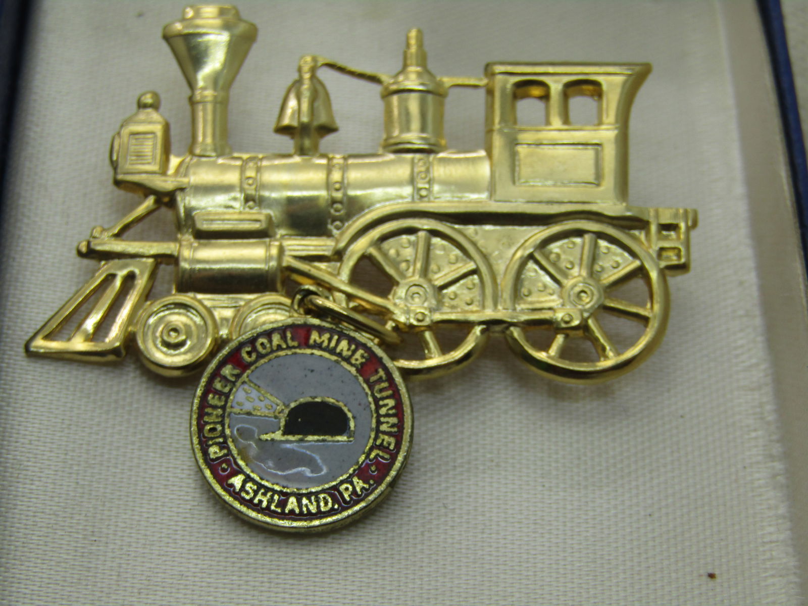 Vintage Pioneer Coal Mine Tunnel, Ashland, PA Train Brooch in Box: Vintage Pioneer Coal Mine Tunnel, Ashland, PA Train Brooch in Box. Gold tone train brook with an enameled dangling charm that is in red behind the lettering that reads "Pioneer Coal Mine Tunnel, Ashla