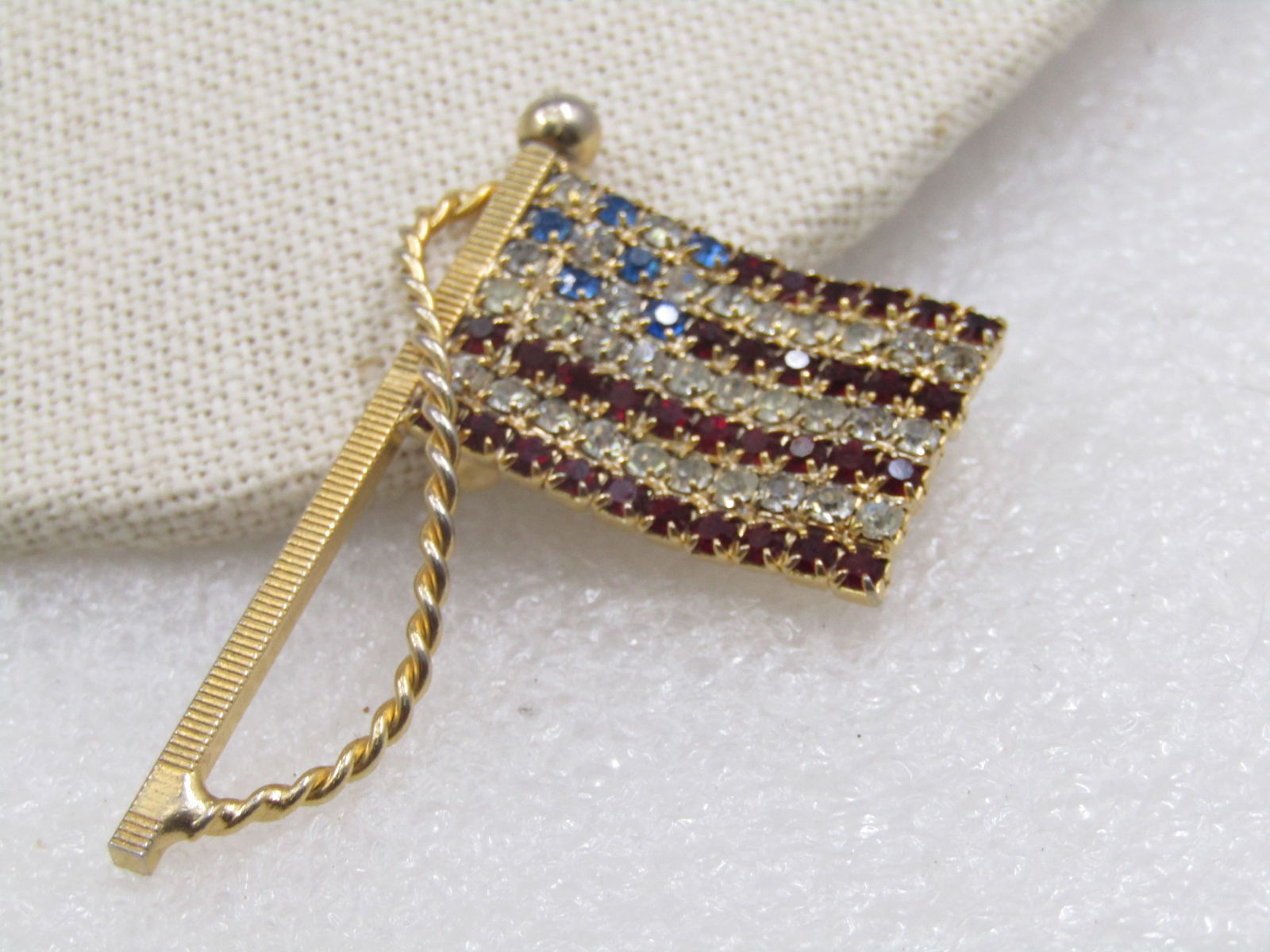 Vintage American Flag Rhinestone Brooch, with Pole, 2": Vintage American Flag Rhinestone Brooch with Pole and rope. 2" tall and slightly over 1" wide with a wavy appearance on the rhinestone flag. 1980's-1990's. This is not signed by the maker. Gold tone a
